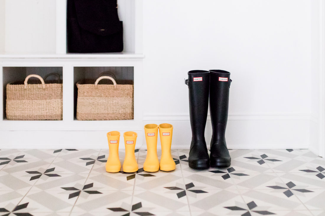 A lineup of black and yellow "Mommy and Me" Hunter boots on the black and white tiled floor of Eva Amurri Martino's Connecticut mudroom