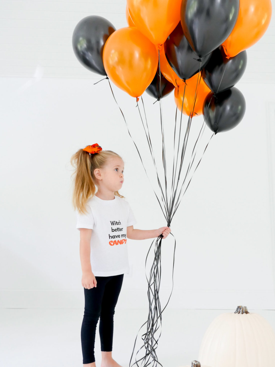 Marlowe Martino wears a festive Halloween tee shirt designed using The Happily App and holds a big bundle of orange and black balloons