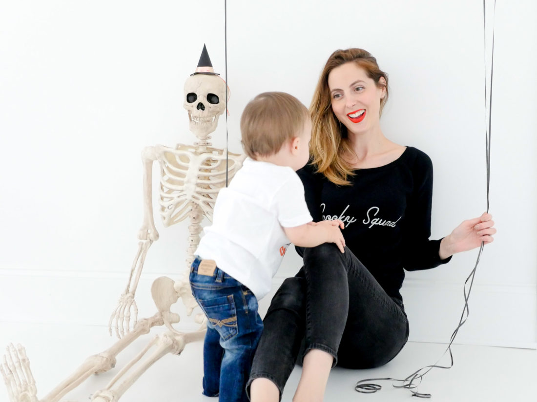 Eva Amurri Martino sits next to a festive skeleton, wearing a custom Halloween themed sweatshirt designed using The Happily App