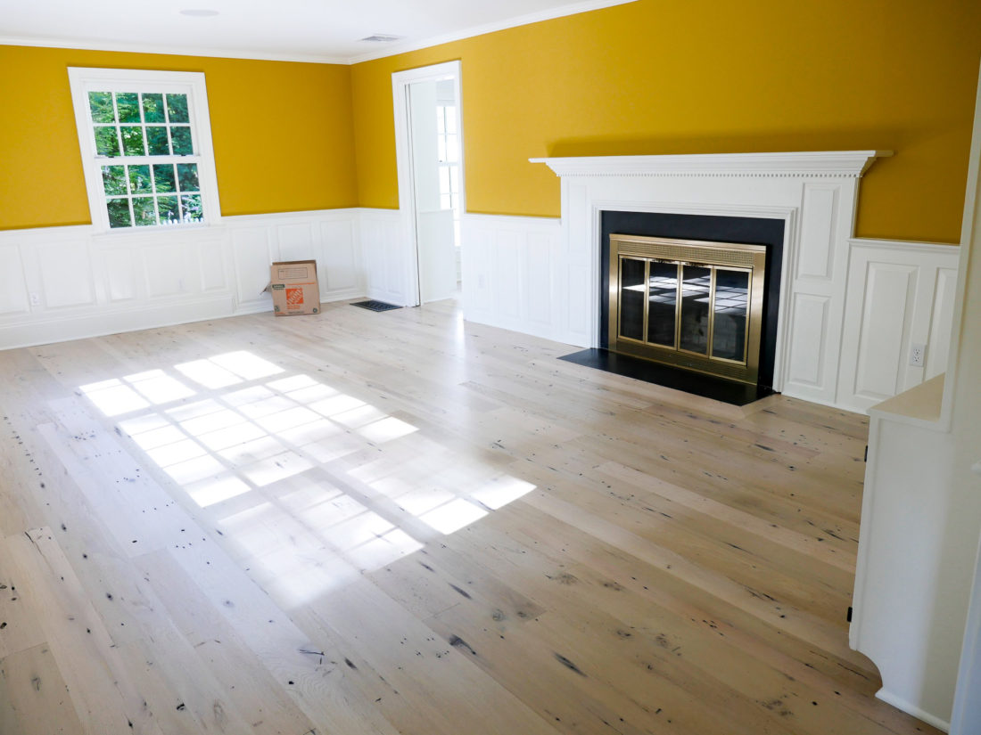 Happily Eva After home in Connecticut with light wood floors, mustard walls and white judge's paneling around the wood burning fireplace in the formal living room. 