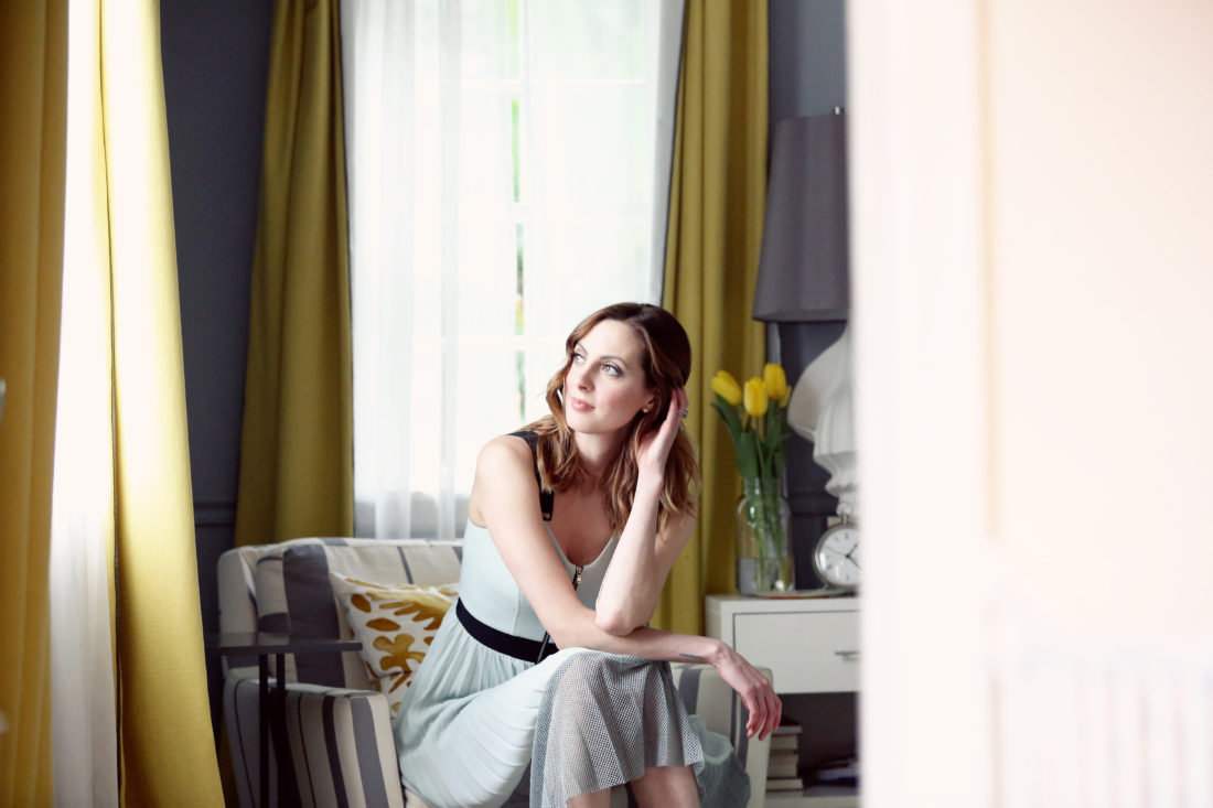 Eva Amurri Martino of the blog Happily Eva After wearing a pale blue dress and sitting on an armchair in the corner of the bedroom, looking out the window