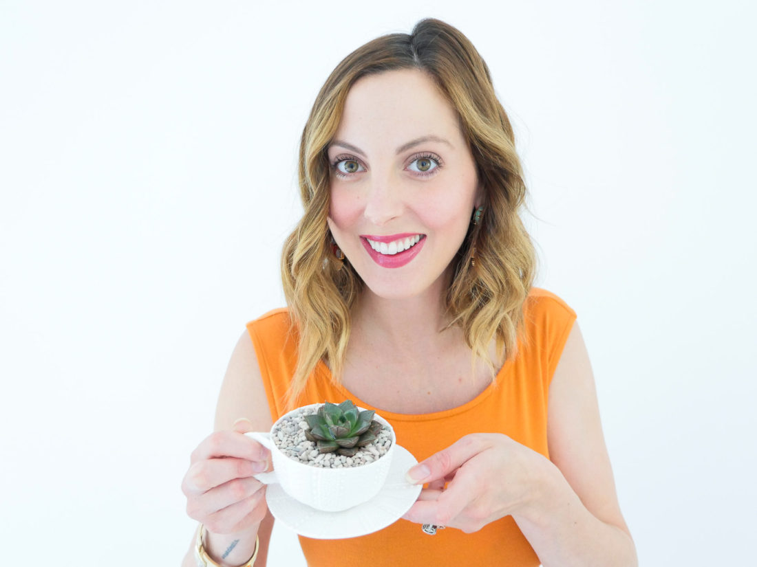 Eva Amurri Martino from the Happily Eva After blog displaying her DIY Teacup Planters with Mini Succulents and small pebbles, wearing a bodycon orange maternity dress and gold bracelet watch