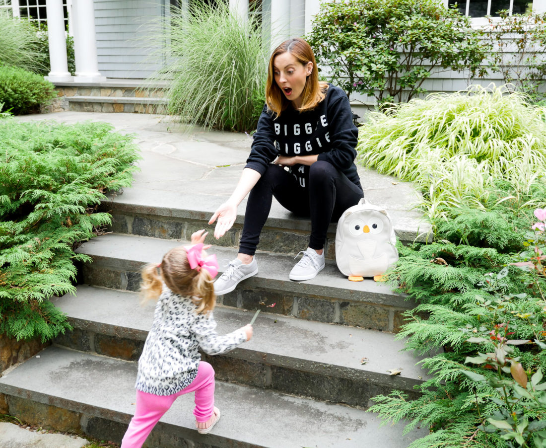 Eva Amurri Martino of lifestyle blog Happily Eva After wearing black maternity leggings and a "biggie biggie biggie can't you see" sweatshirt with her daughter Marlowe on the steps of their home in connecticut