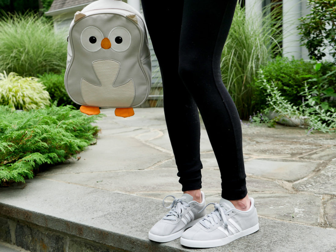 Eva Amurri Martino of lifestyle blog Happily Eva After wearing black maternity leggings and adidas sneakers holding her daughter's grey owl backpack