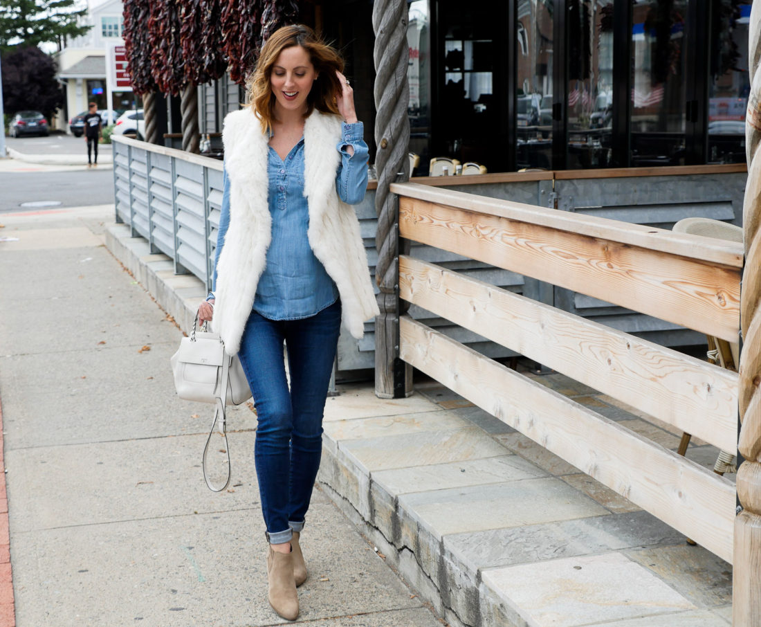 Eva Amurri Martino of lifestyle blog Happily Eva After wearing dark denim maternity jeans, a light chambray maternity top, white vest, and light brown western style booties walking down the street in connecticut