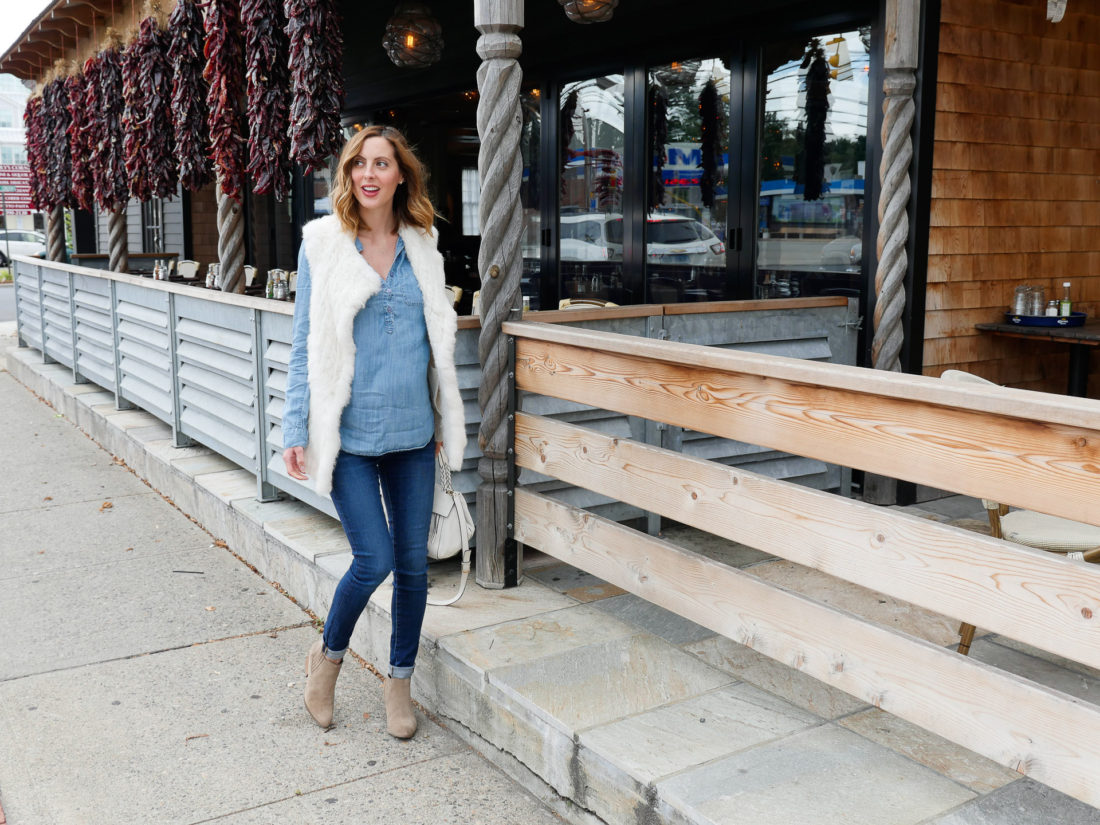 Eva Amurri Martino of lifestyle blog Happily Eva After wearing dark denim maternity jeans, a light chambray maternity top, white vest, and light brown western style booties walking down the street in connecticut