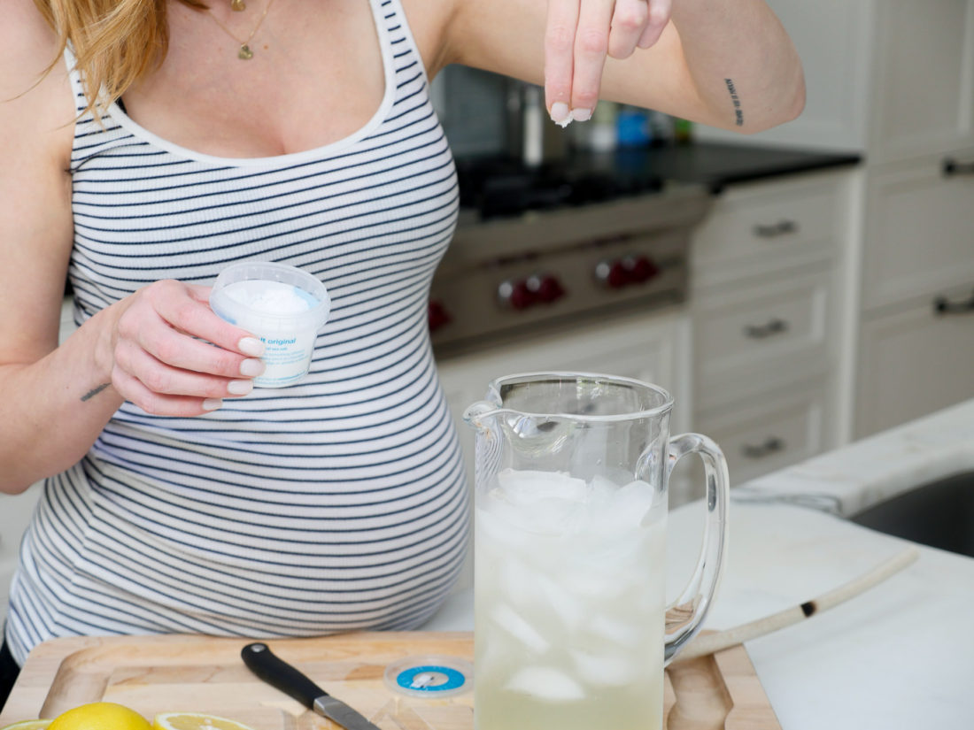 Eva Amurri Martino of lifestyle blog Happily Eva After adding salt to a glass pitcherin her kitchen to make a hydrating laborade for her Home Birth