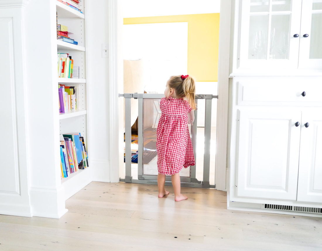 Marlowe Martino wearing a red and white checkered dress and a high ponytail trying to open the new safety gate installed by eva amurri martino in their new connecticut home