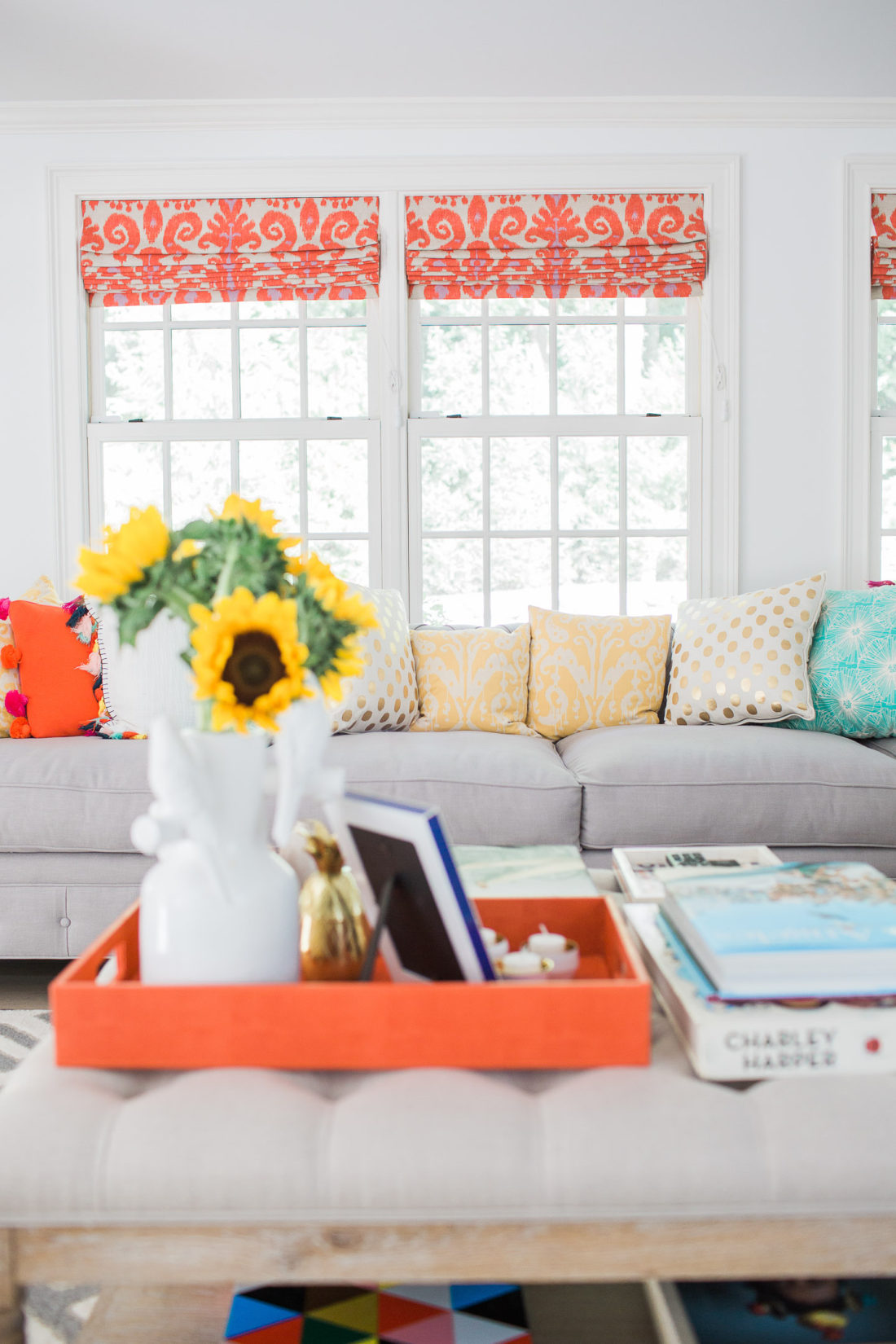 A colorful view of Eva Amurri Martino's Family room couch and coffee table ottoman with custom orange and magenta ikat roman shades