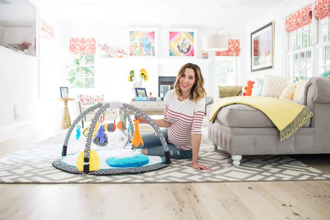 Eva Amurri Martino of lifestyle blog Happily Eva After sitting on the floor of her colorful family room with the fisher price by Jonathan Adler sensory gym 