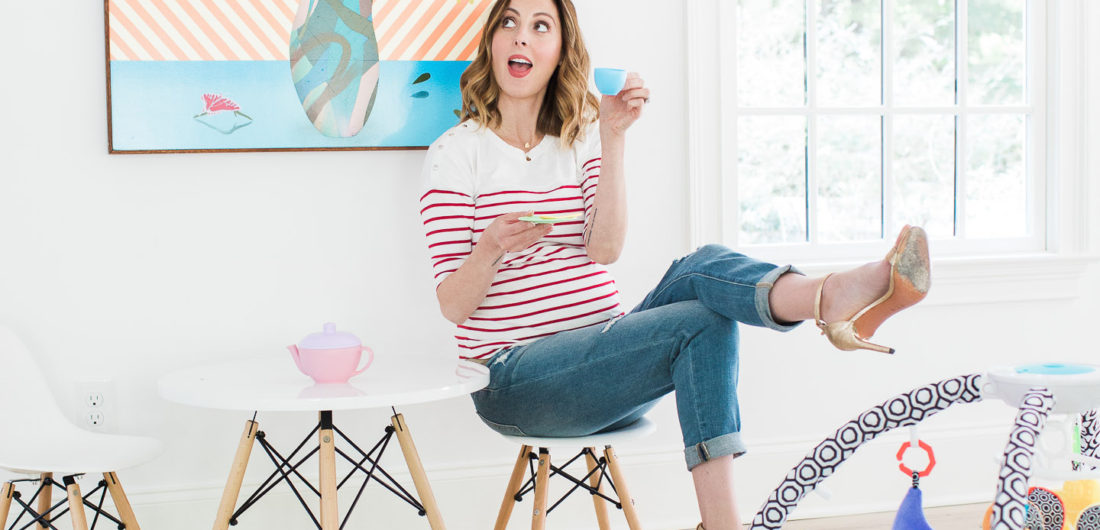 Eva Amurri Martin of lifestyle blog Happily Eva After drinking tea from her daughter's tea set and perching on a tiny white midcentury modern playroom furniture set with the jonathan adler crafter by fisher price collection sensory gym in the foreground