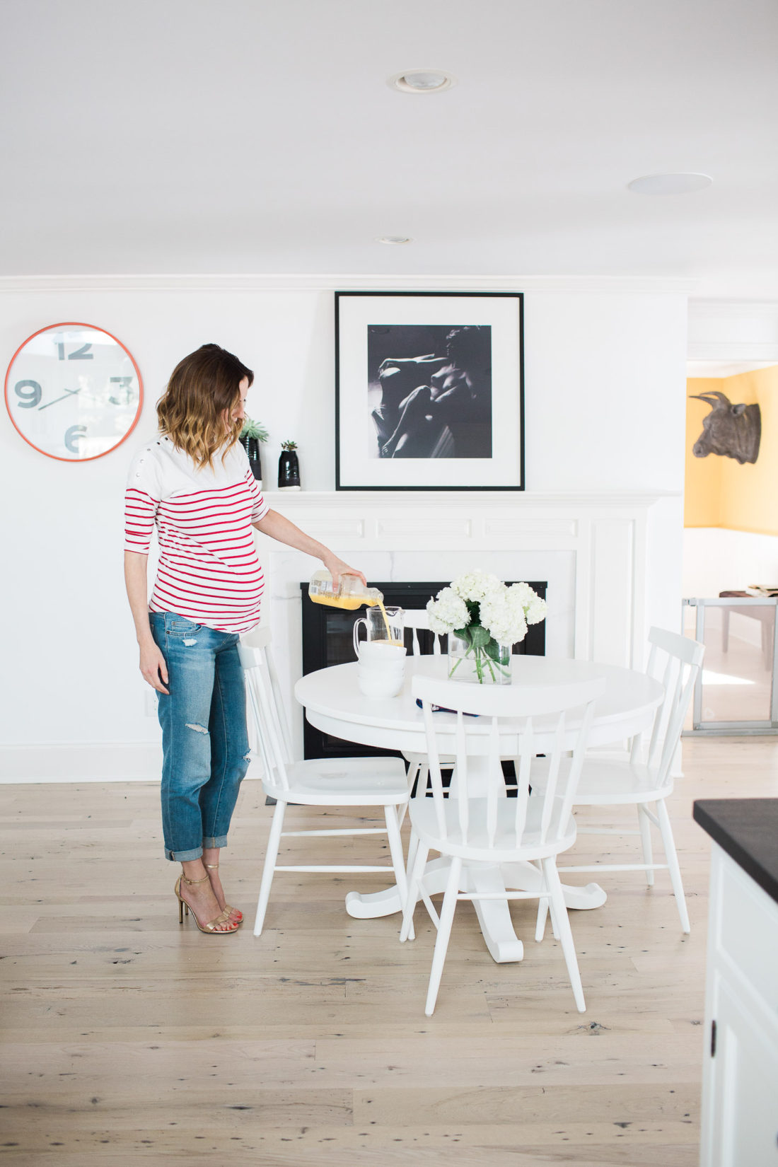 Eva Amurri Martino of lifestyle blog Happily Eva After pouring orange juice while wearing a red and white striped maternity top in her kitchen in connecticut