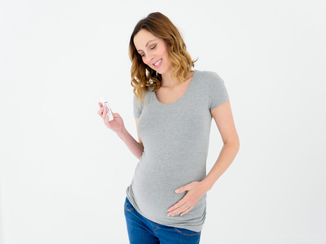 Eva Amurri Martino of lifestyle blog Happily Eva After wearing a grey maternity shirt and maternity jeans at 37 weeks pregnant and cradling her baby bump