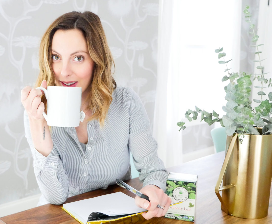 Eva Amurri Martino of lifestyle blog Happily Eva After takes time for herself by writing in a journal and sipping raspberry leaf tea from a white mug in her bright dining room