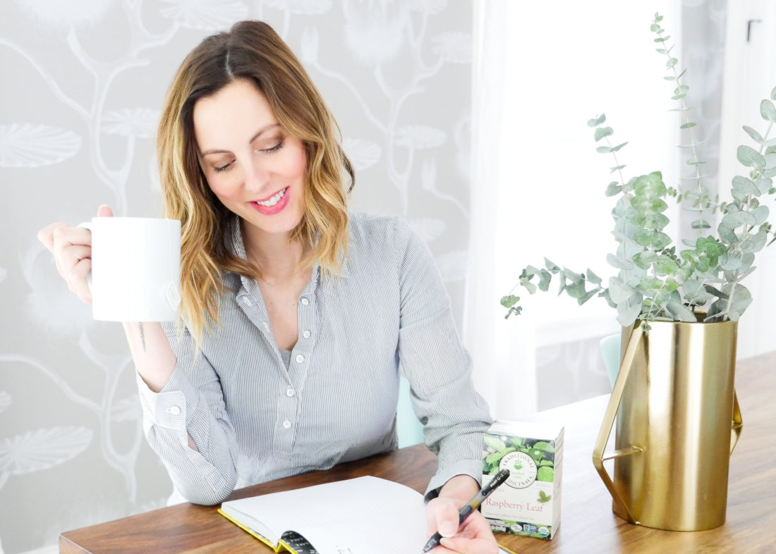 Eva Amurri Martino of lifestyle blog Happily Eva After takes time for herself by writing in a journal and sipping raspberry leaf tea from a white mug in her bright dining room