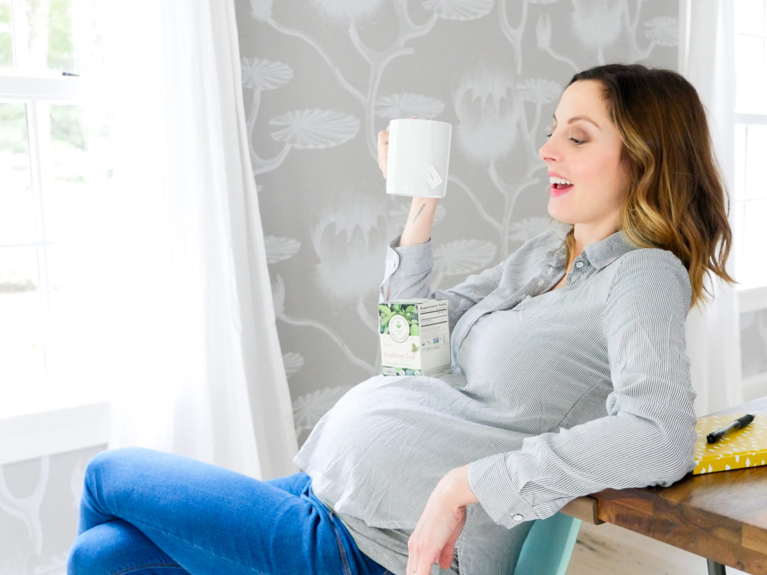 EVa Amurri Martino at 38 weeks pregnant, sipping from a mug of tea wearing a white and navy striped maternity shirt and blue jeans