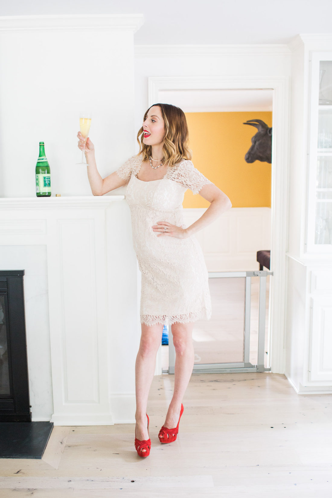 Eva Amurri Martino of lifestyle and motherhood blog Happily Eva After, standing in a champagne colored lace dress and red louboutin platform pumps, holding a glass of sparkling cider in a celebratory toast