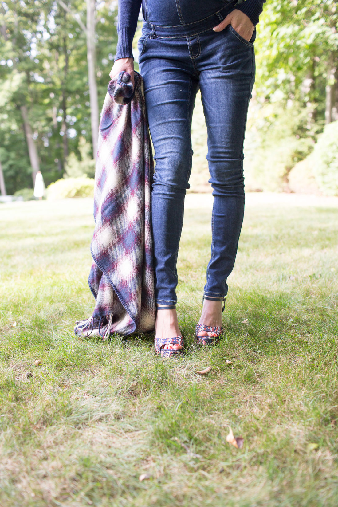 Eva Amurri Martino of lifestyle blog Happily Eva After standing in her yard in maternity overalls, a navy felt hat, and a plaid poncho at her home in connecticut