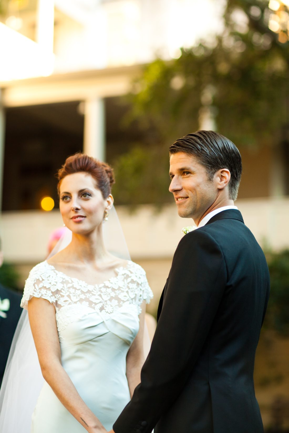 Eva Amurri Martino of lifestyle and motherhood blog Happily Eva After, wearing a white wedding dress with flower applique detail while holding hands with husband Kyle Martino wearing a black Brioni Tuxedo in Charleston South Carolina