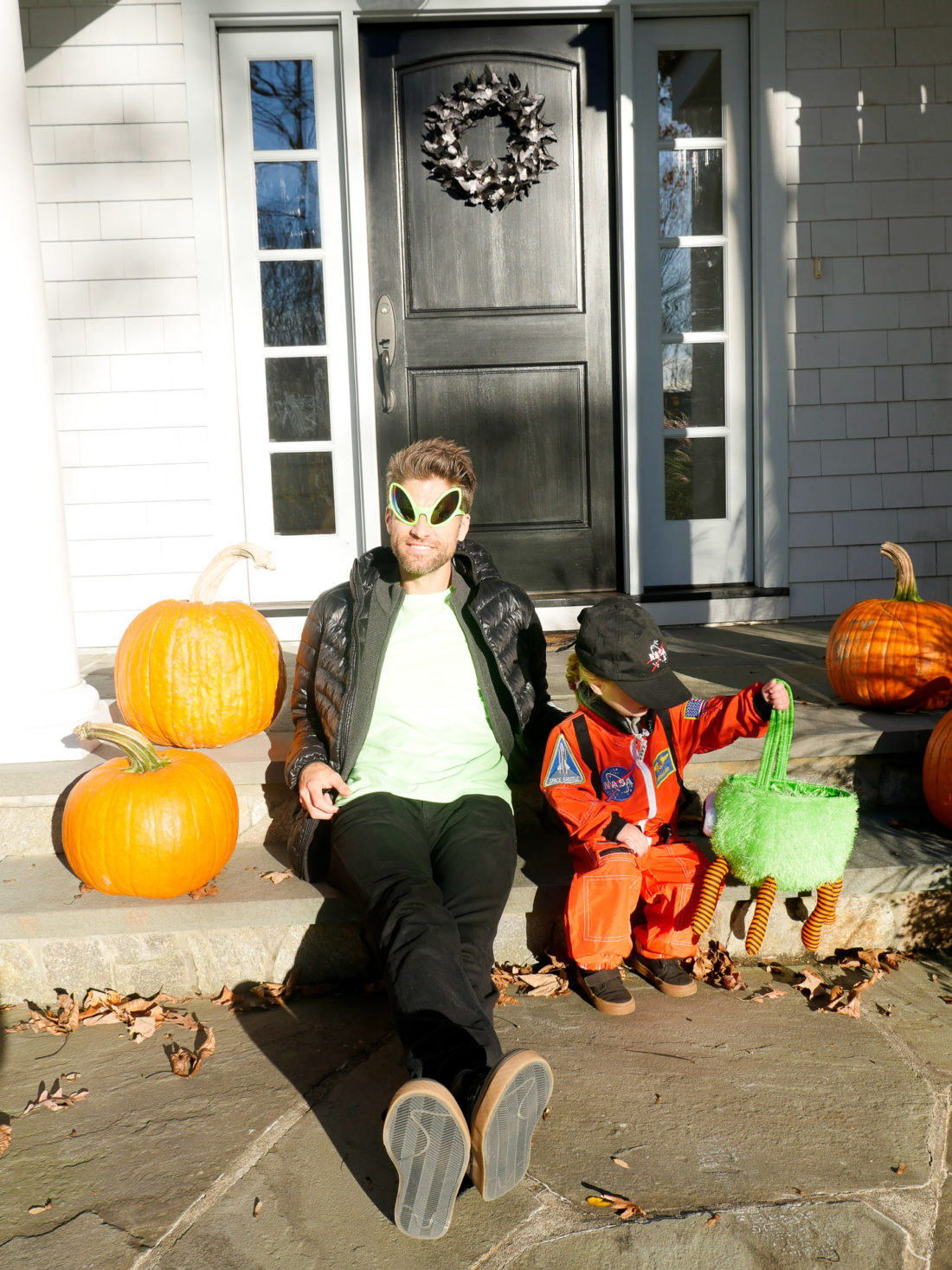 Kyle Martino and Marlowe Martino, sitting on the steps of their Connecticut home dressed as an Alien and an Astronaut for Halloween