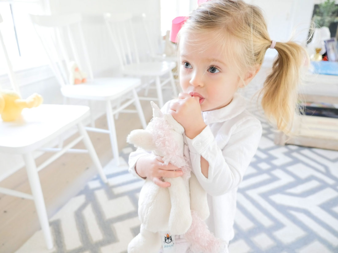 Marlowe Martino, wearing a white top and bright pink bow, clutching a stuffed unicorn