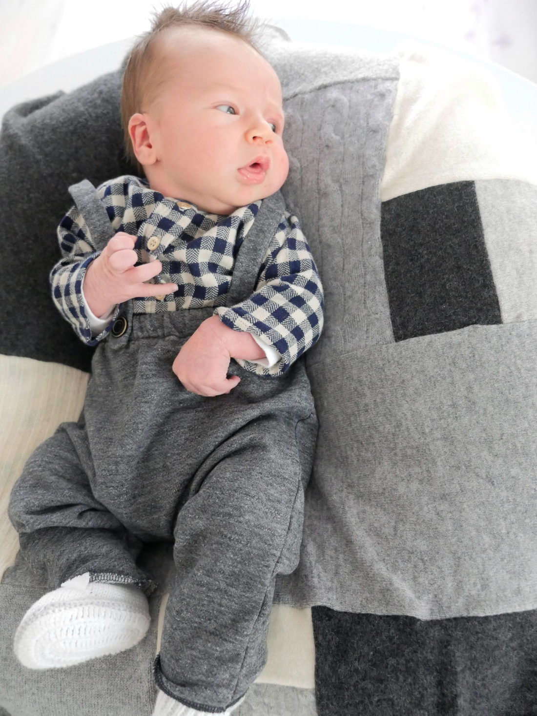 Major James Martino wearing grey overalls and a black and white checked shirt laying on a grey patchwork cashmere blanket