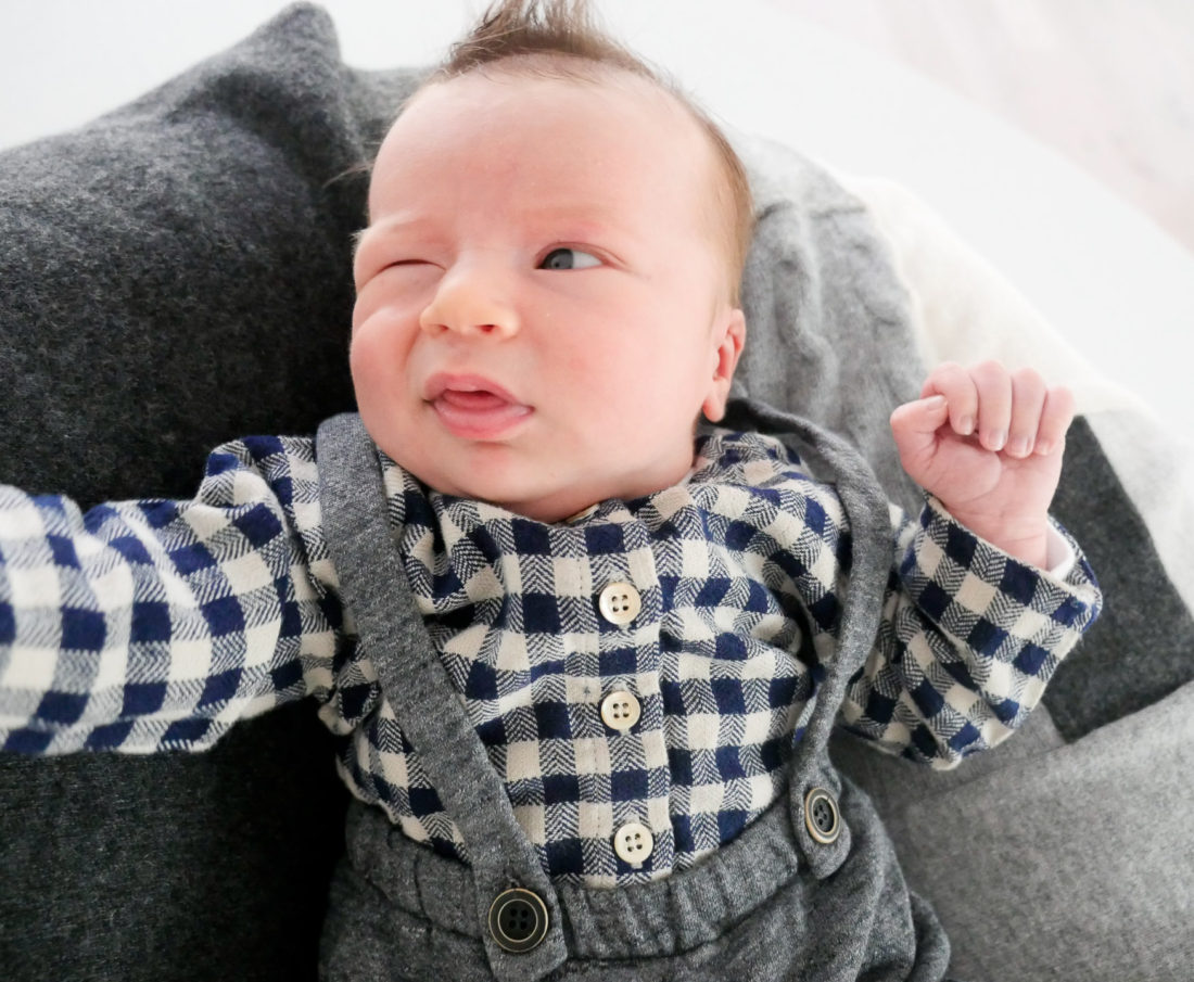 Major James Martino wearing grey overalls and a black and white checked shirt laying on a grey patchwork cashmere blanket