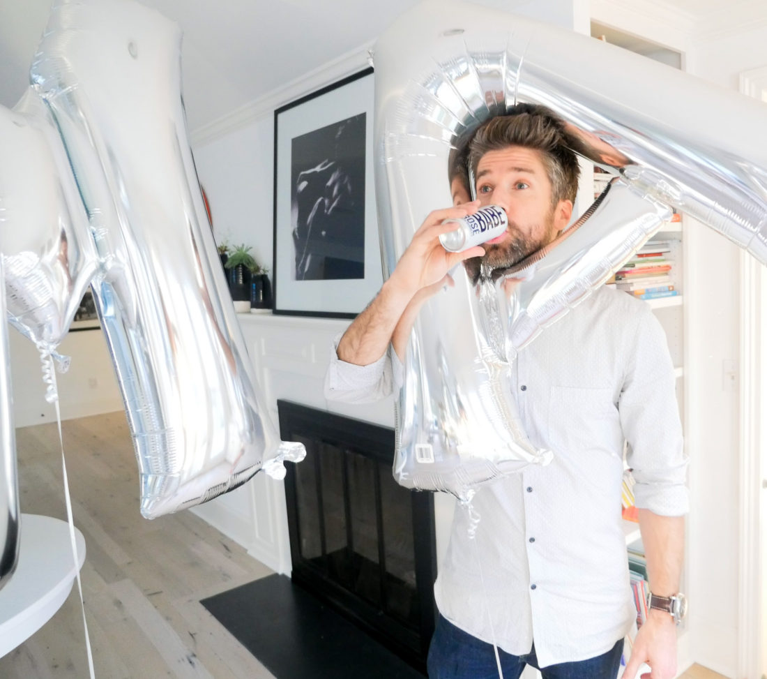 Kyle Martino, wearing a black and white button down shirt and drinking from a can of Babe Rose with Bubbles