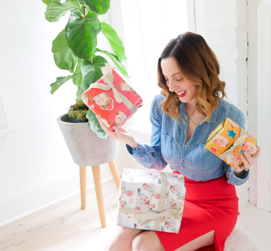 Eva Amurri Martino of lifestyle and motherhood blog Happily Eva After, wearing a red skirt and chambray top and holding wrapped holiday gifts with her children's faces on them