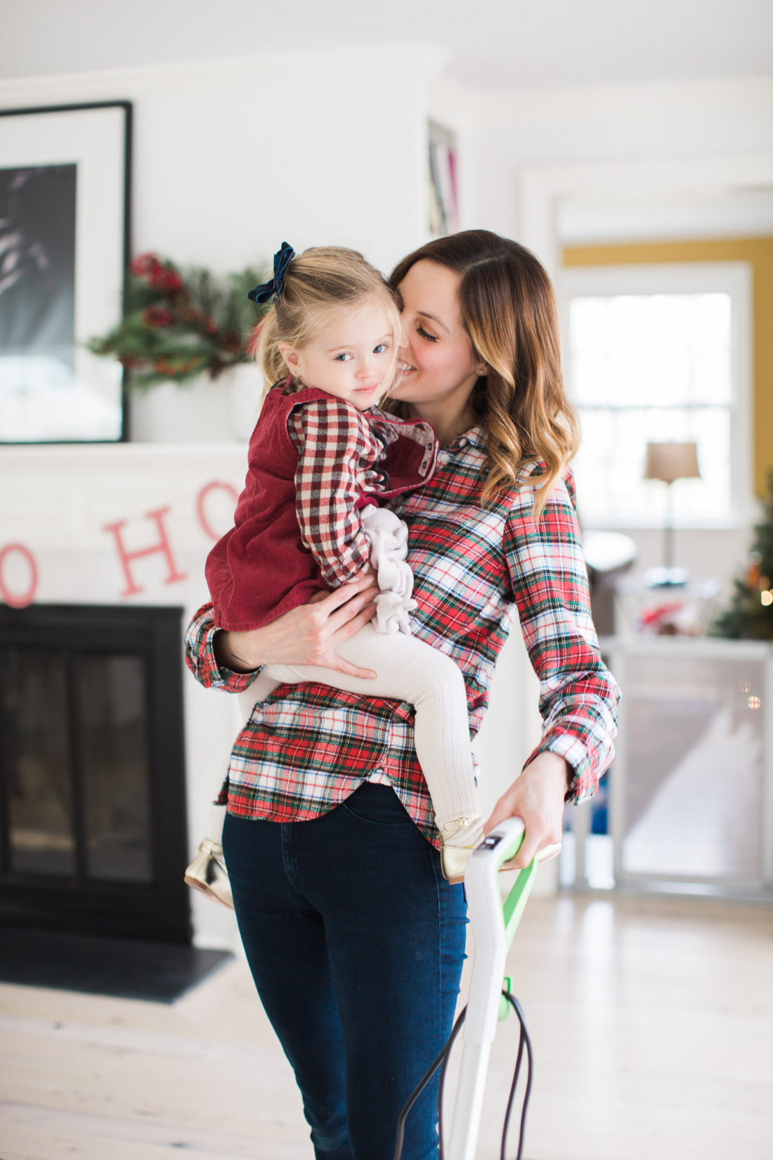 Eva Amurri Martino of lifestyle and motherhood blog Happily Eva After holds her toddler daughter Marlowe in her arms while she vacuums her home and prepares for holiday parties