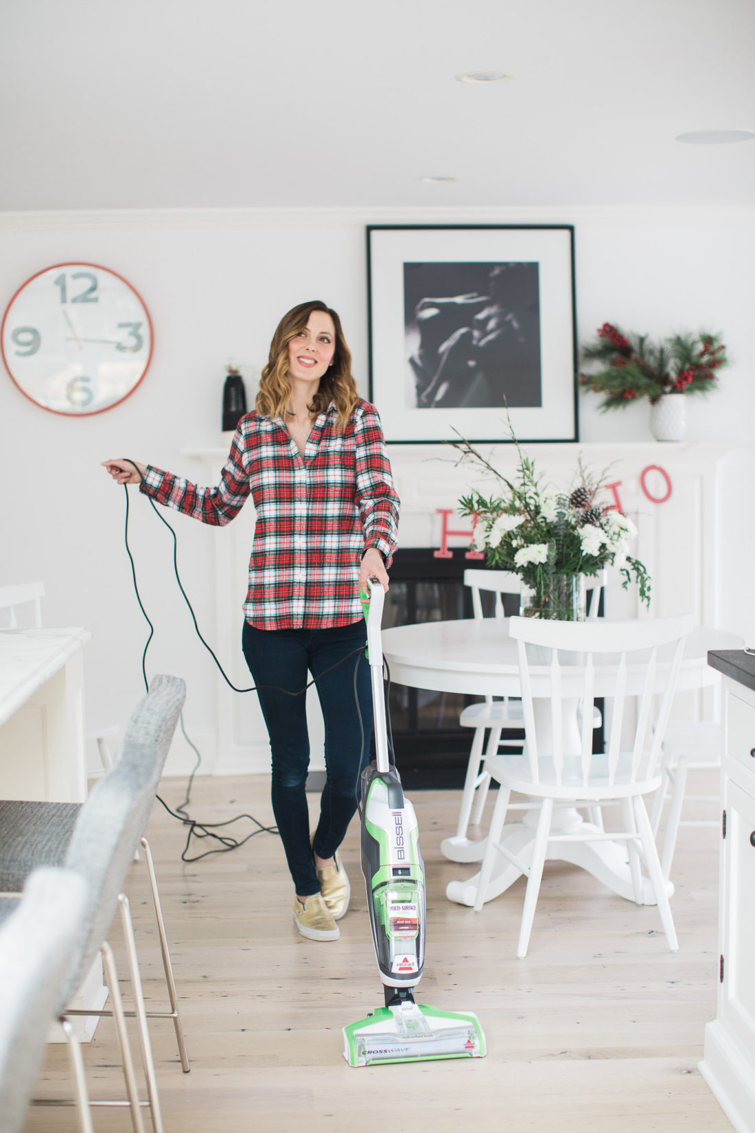 Eva Amurri Martino vacuums in her kitchen wearing a plain flannel shirt and blue jeans