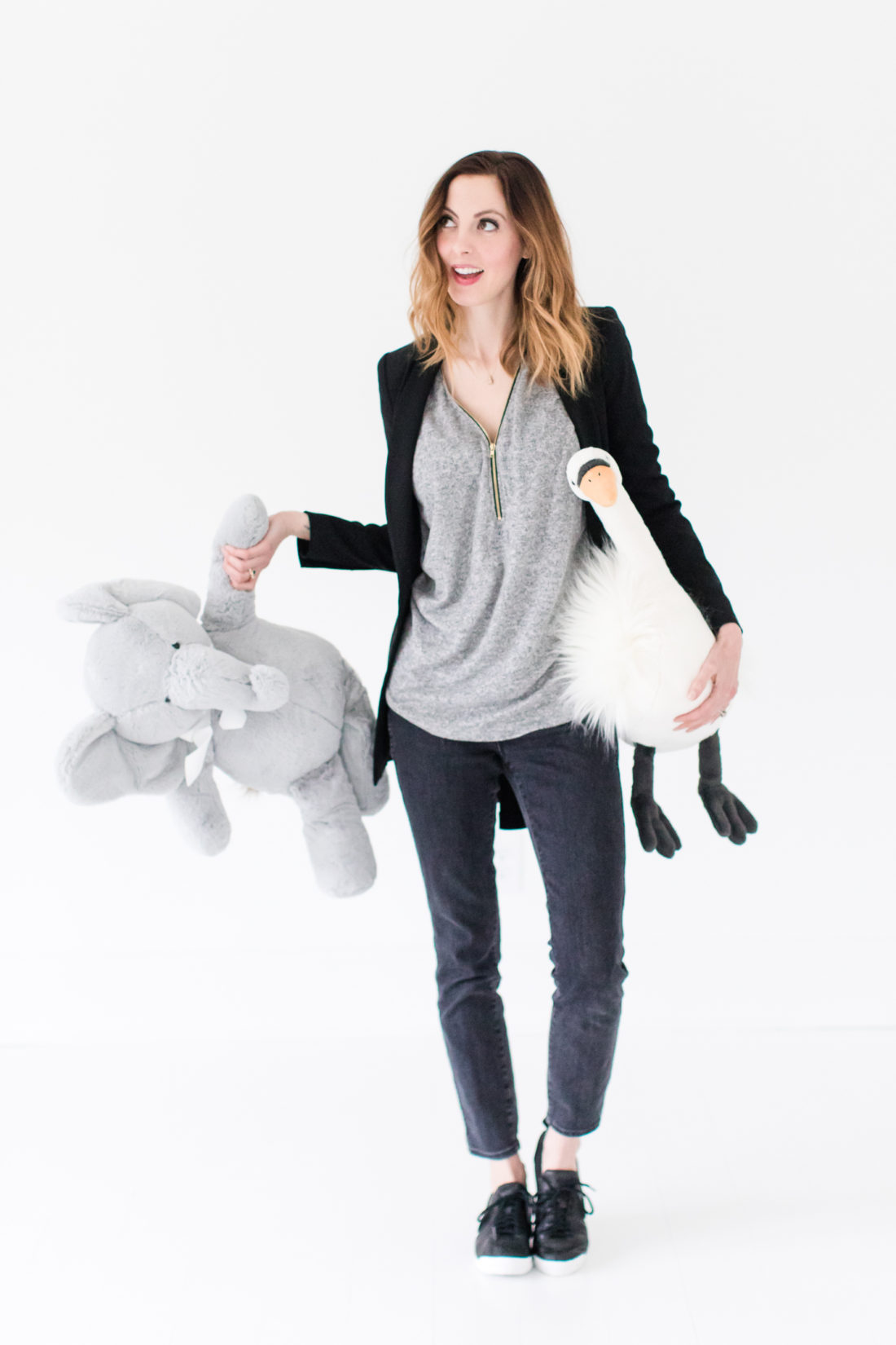 Eva Amurri Martino wears black jeans, a grey top, black nike sneakers, and a black fitted blazer as she cleans up toys in her studio