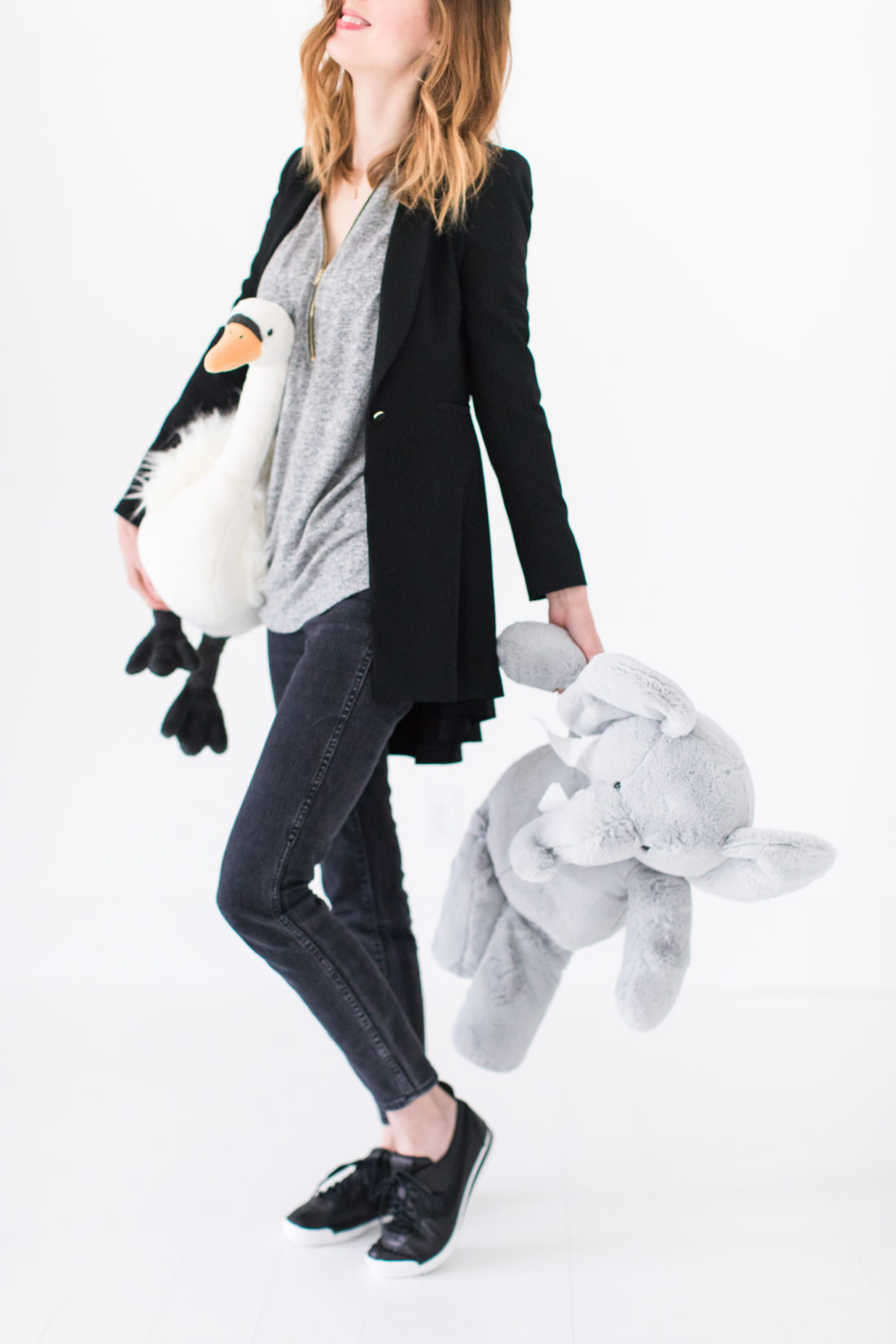 Eva Amurri Martino cleans up stuffed animals wearing a pair of high waisted jeans, a black blazer, and black leather sneakers