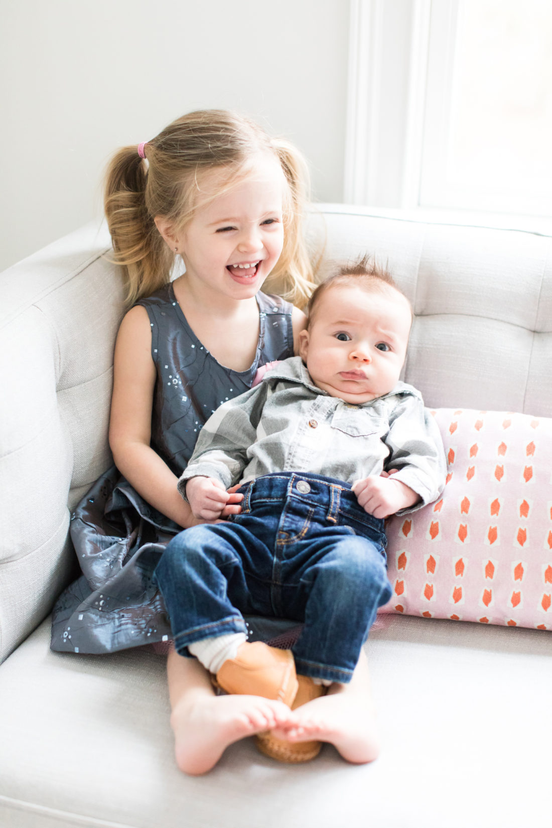 Marlowe Martino holds baby brother, Major, while wearing a sparkly grey dress and pigtails