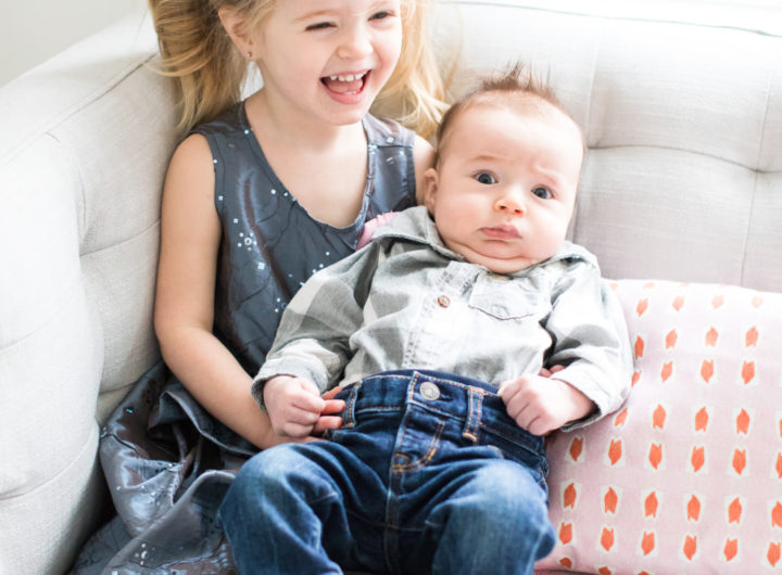 Marlowe Martino holds baby brother, Major, while wearing a sparkly grey dress and pigtails