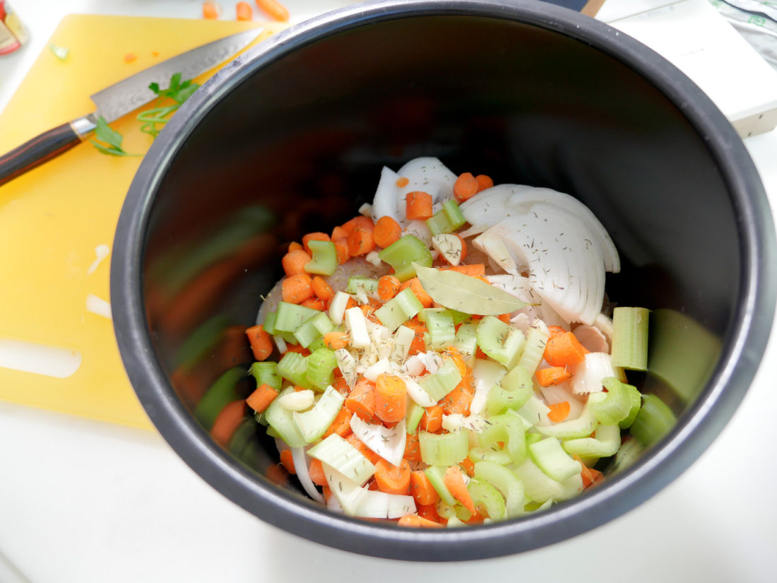 chopped vegetables and other ingredients wait in the crockpot to be made in to chicken noodle soup