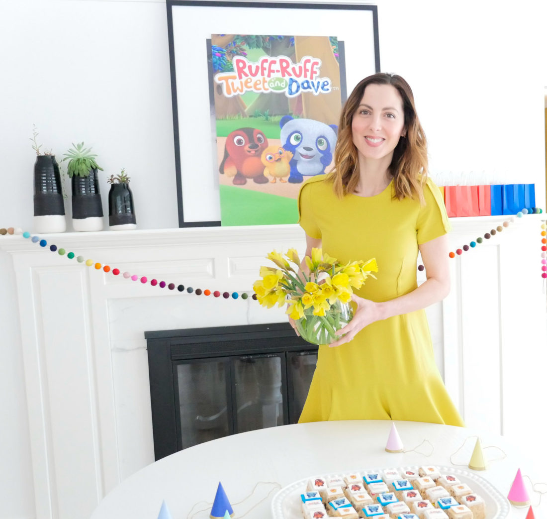 Eva Amurri Martino holds a vase of daffodils, wearing a yellow dress, for a post about entertaining for children