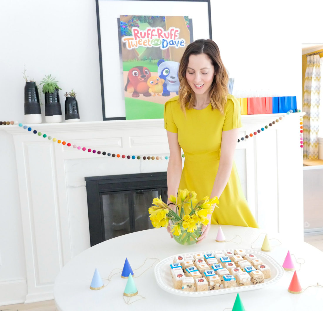 Eva Amurri Martino holds a vase of daffodils, wearing a yellow dress, for a post about entertaining for children