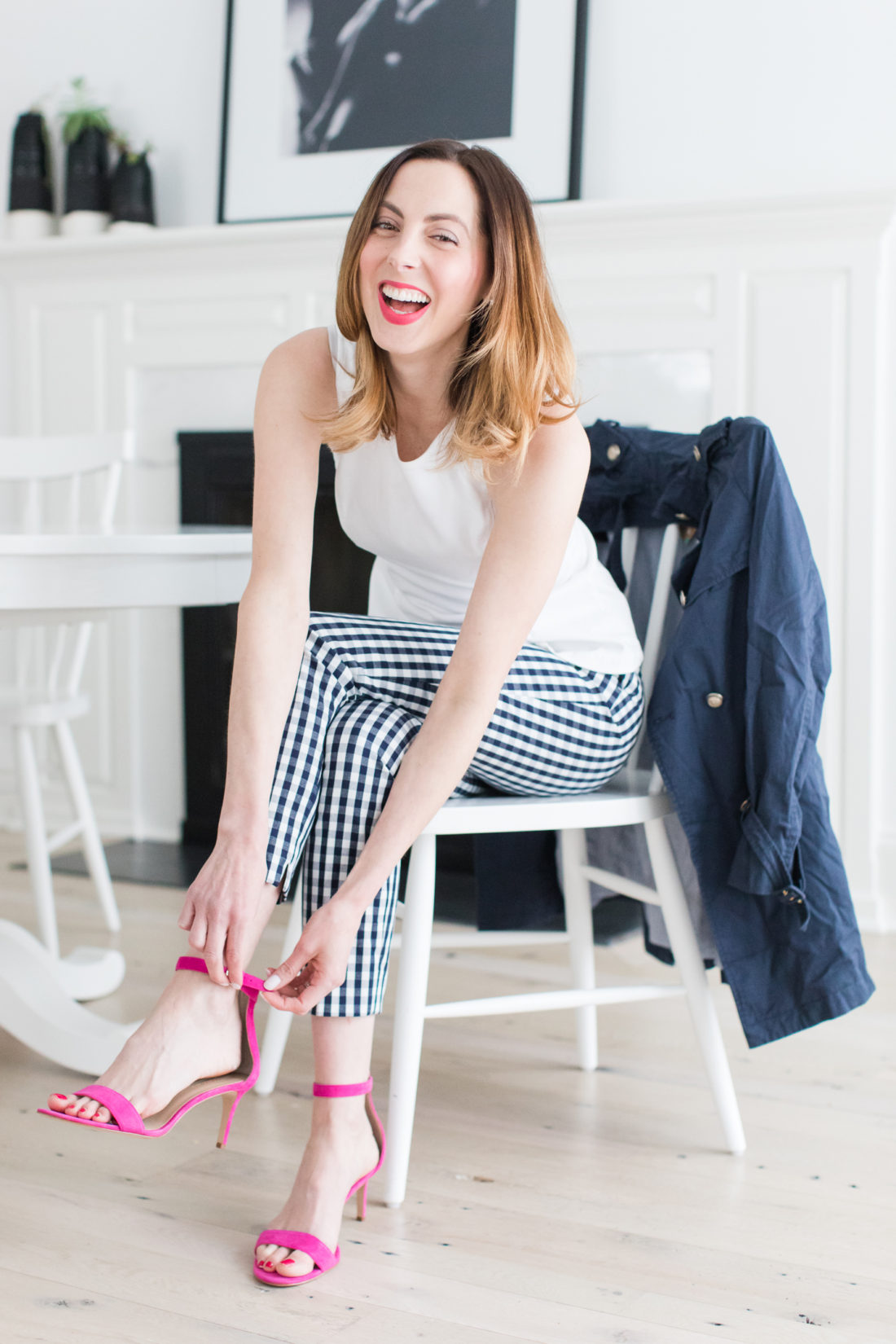 Eva Amurri Martino wears navy and white gingham pants, a white top, and fastens her hot pink heels at the kitchen table