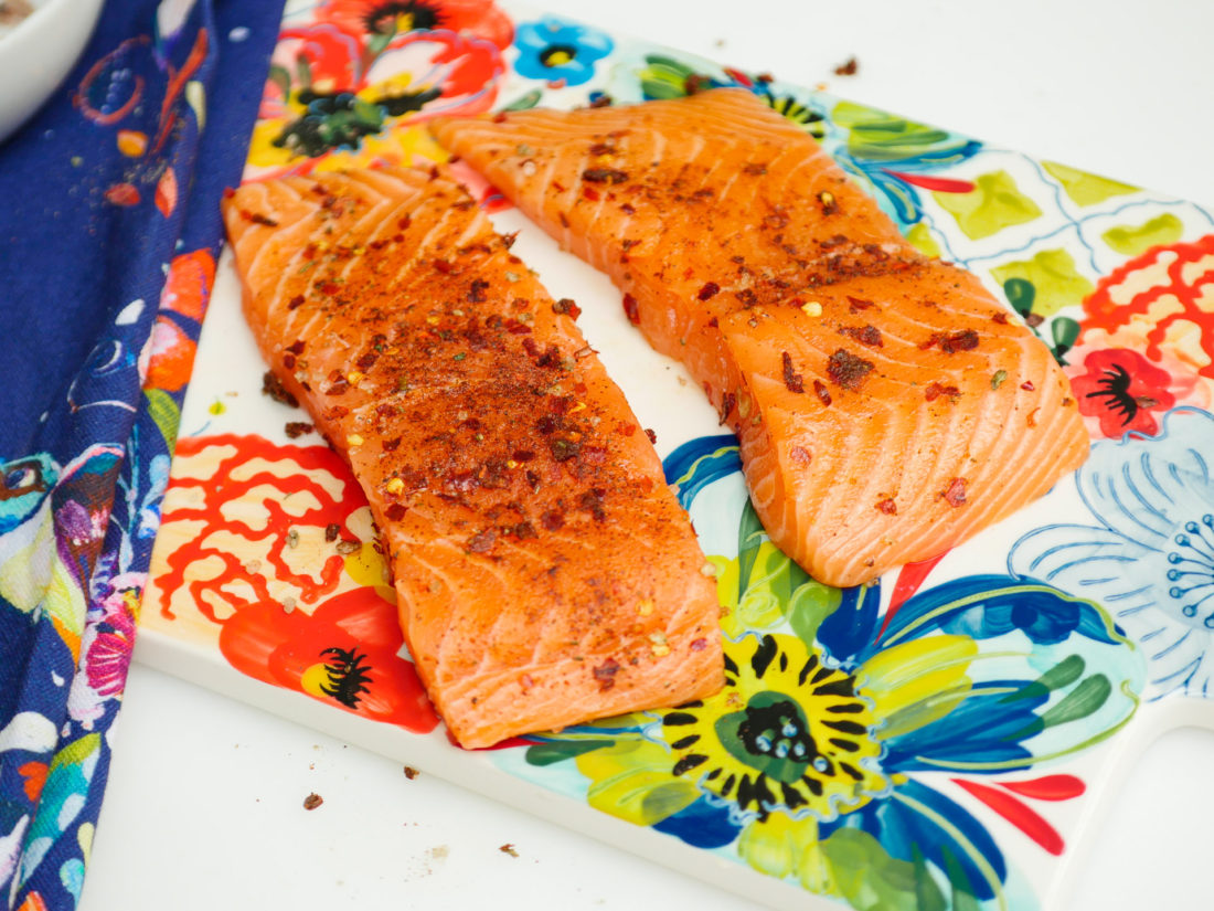 Raw salmon sits on the colorful cutting board with the Mexican Spice rub applied