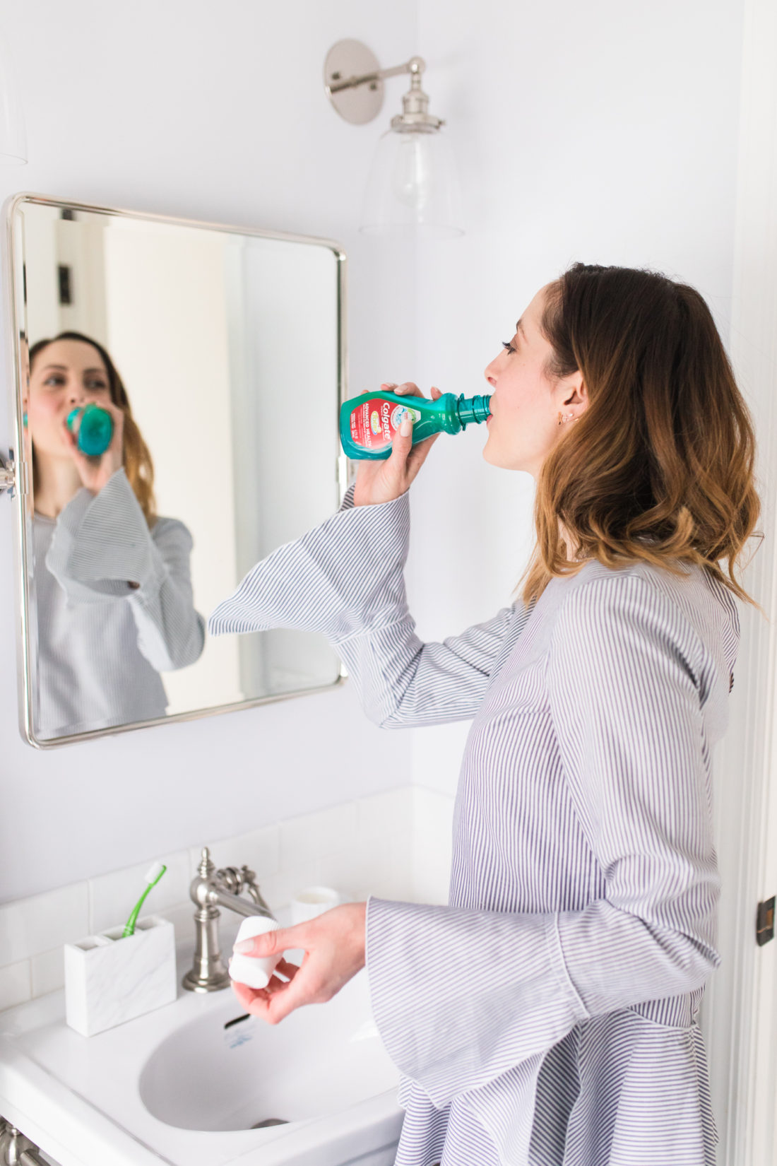 Eva Amurri Martino wears a white and blue pinstripe top and tags a swig of Colgate mouthwash in the bathroom of her Connecticut home