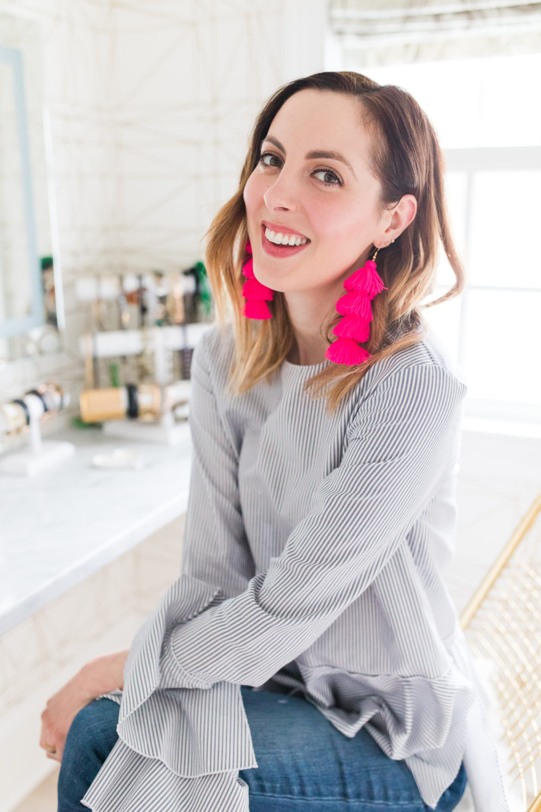 Eva Amurri Martino wears a blue and white pinstripe bell sleeve top and bright pink tassel earrings