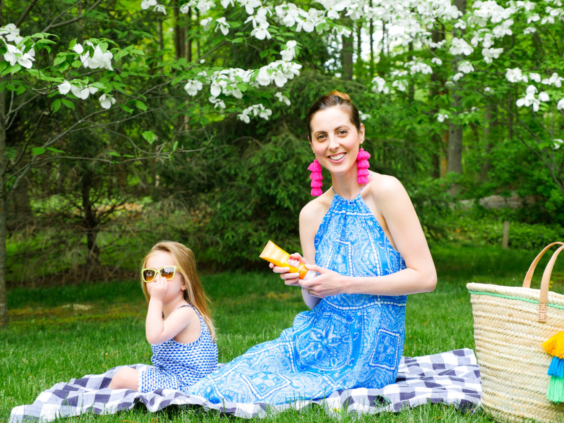 Eva Amurri Martino and daughter Marlowe sit on a picnic blanket on the grass and apply sunscreen