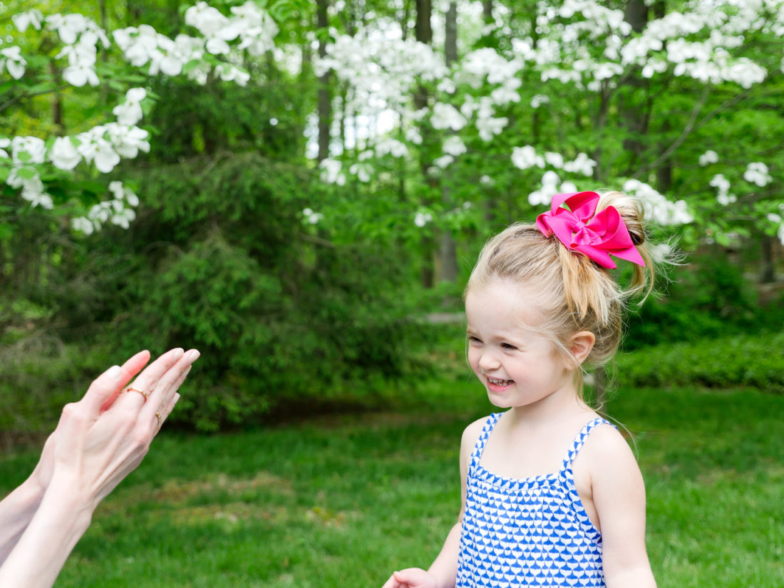 Marlowe Martino wears a blue and white dress and a magenta bow, and gets sunscreen applied to her face