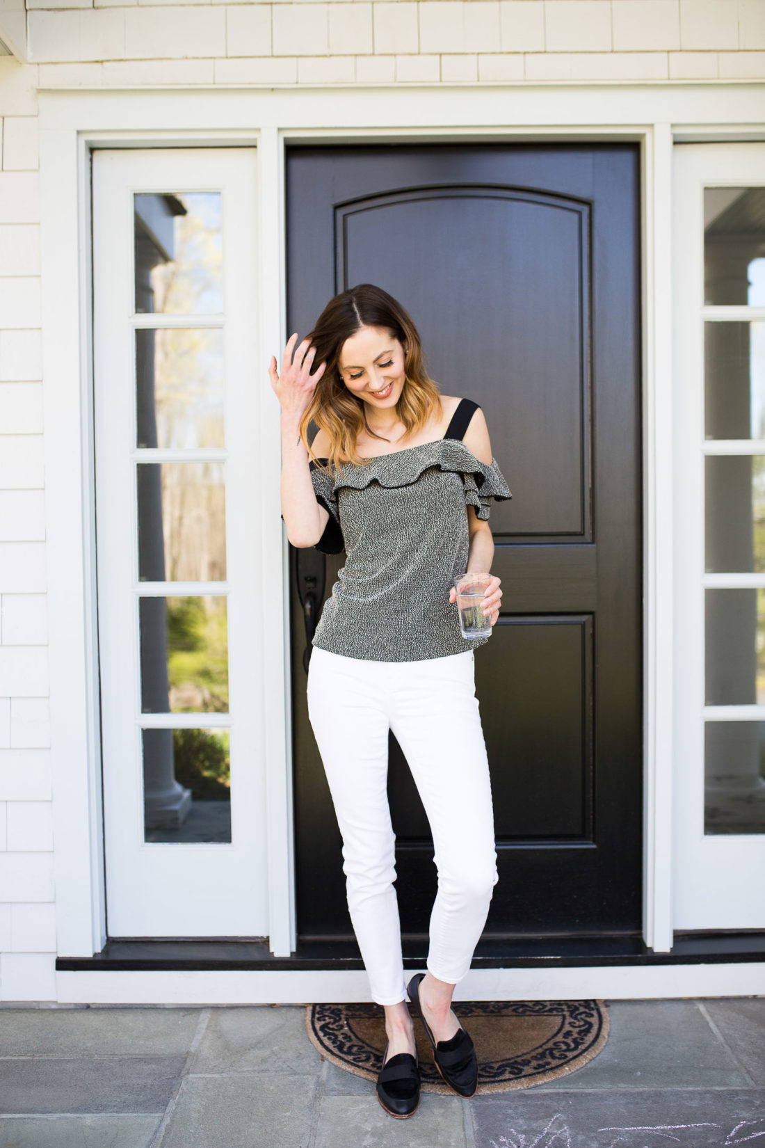 Eva Amurri Martino wears a black top and white jeans in front of her Connecticut home