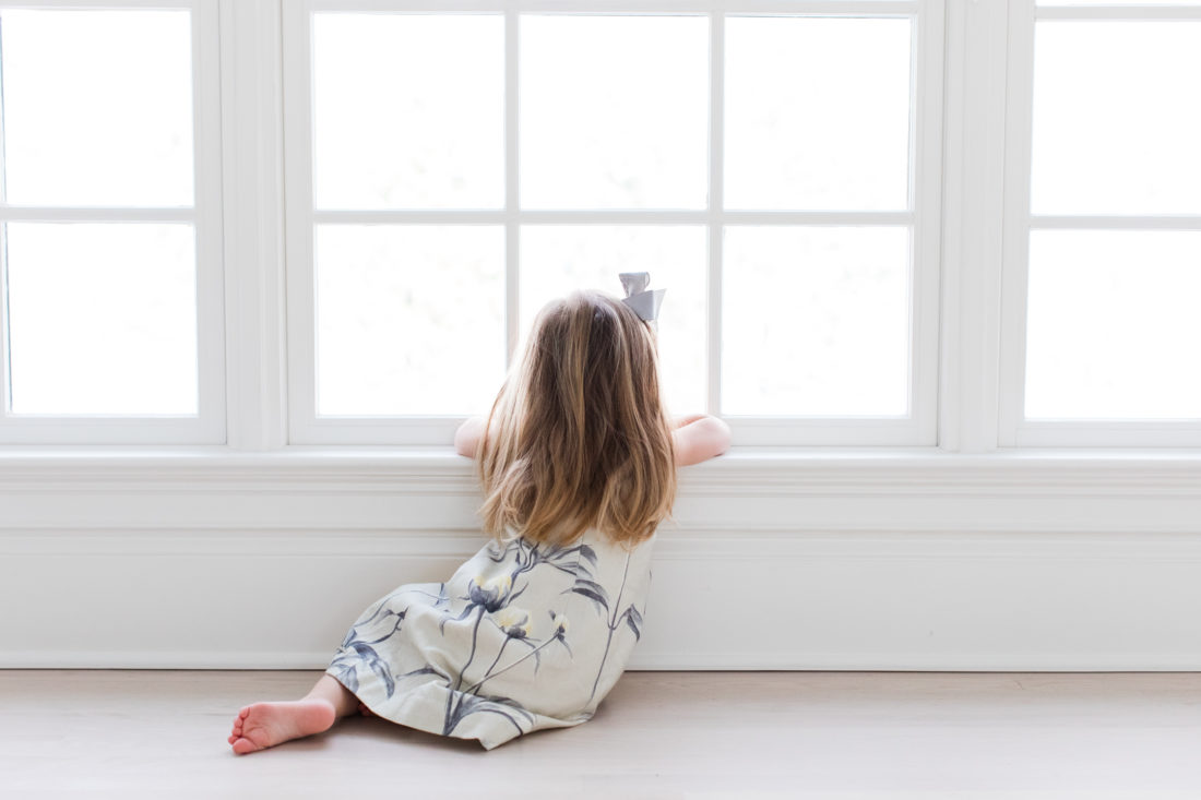 Marlowe Martino wears a floral dress and grey hair bow and looks out the window