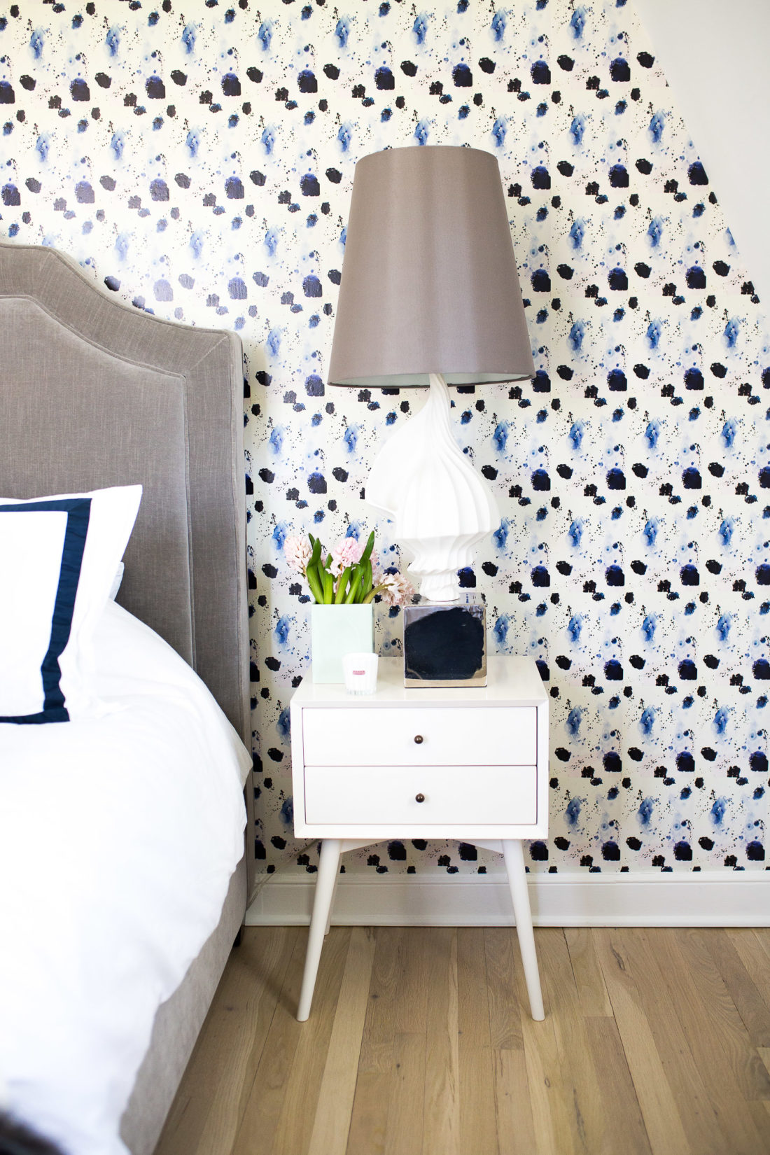 Eva Amurri Martino shows off her guest room revamp, featuring crisp navy and white sheets, midcentury modern bedside tables, a jonathan adler lamp, and kerri rosenthal wallpaper.