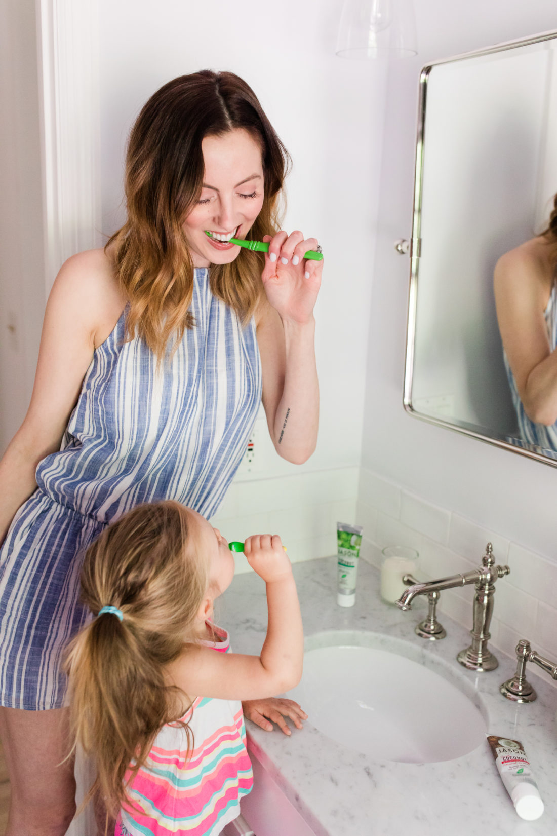 Eva Amurri Martino wears a blue and white striped romper and brushes her teeth with two year old daughter, Marlowe, in the bathroom of their Connecticut home
