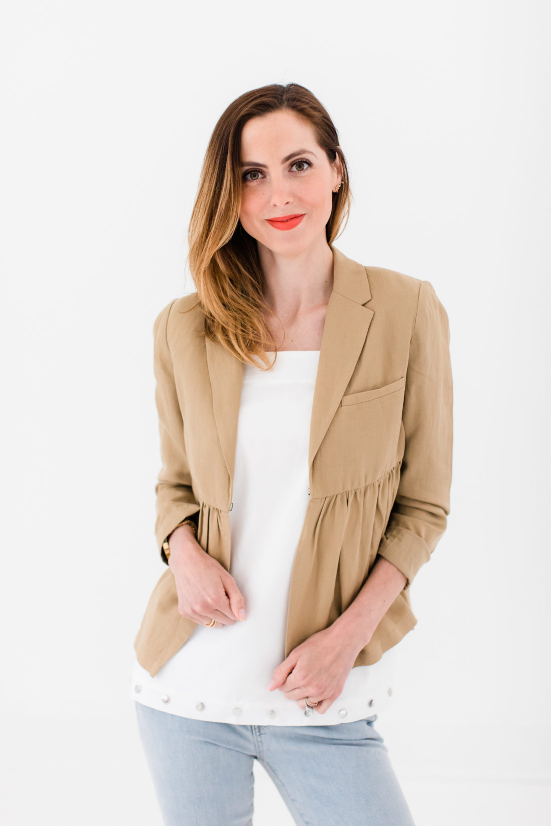 Eva Amurri Martino wears a white bow top, camel ruffle jacket, and jeans as part of a post about packing simply