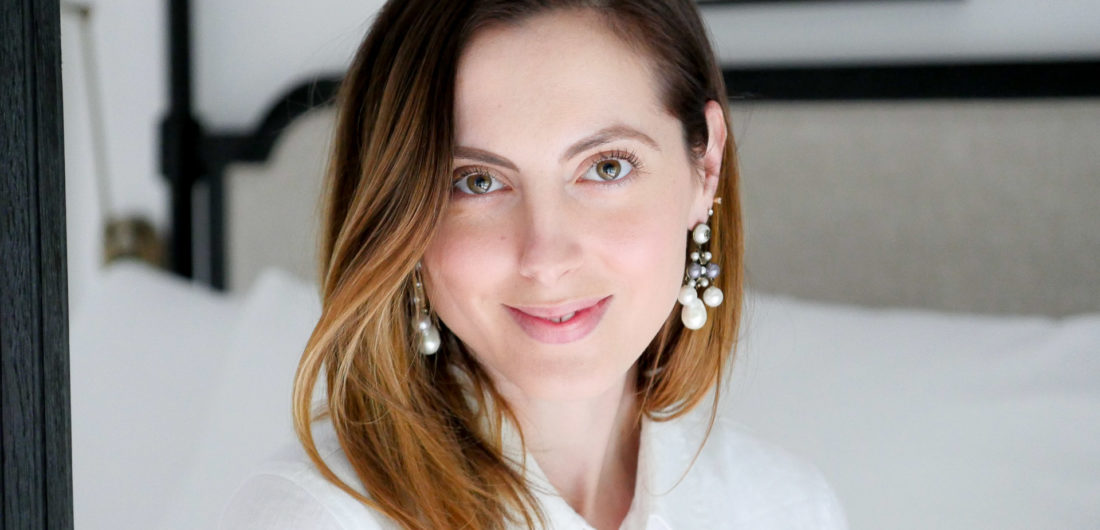 Eva Amurri Martino sits on her bed wearing a white shirt dress, in an "after" pic from using SKII Facial Treatment Essence